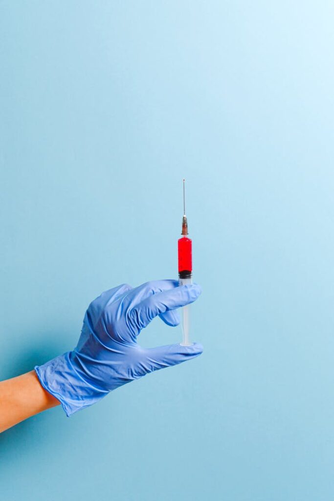 A gloved hand holds a syringe with red liquid, set against a blue background.